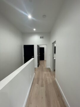 Narrow hallway with wooden floor and open doors.