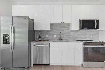 Shiny modern kitchen with stainless steel refrigerator, microwave, oven, and white cabinetry.