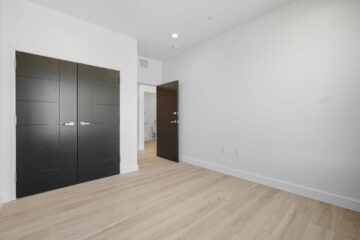 Modern minimalist bedroom with black double doors and light wood flooring.