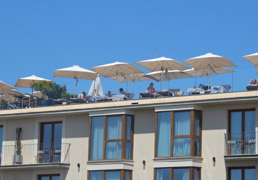 People relaxing under umbrellas on hotel rooftop.
