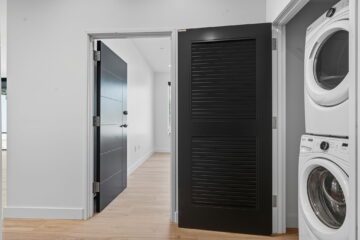 Modern laundry room with stacked washer and dryer, black storage cabinet, and light wood flooring.